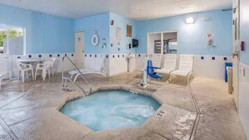 A swimming pool area with a hot tub, lounge chairs, and a small seating area with tables.