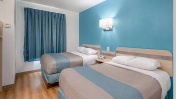 Une chambre d’hôtel avec deux lits, une table de chevet avec un téléphone, une fenêtre avec des rideaux et un luminaire fixé au mur.