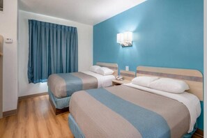 Une chambre d’hôtel avec deux lits, une table de chevet avec un téléphone, une fenêtre avec des rideaux et un luminaire fixé au mur.