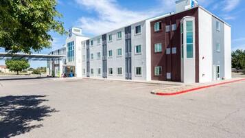 En moderne bygning med fladt tag, store vinduer og en parkeringsplads foran.