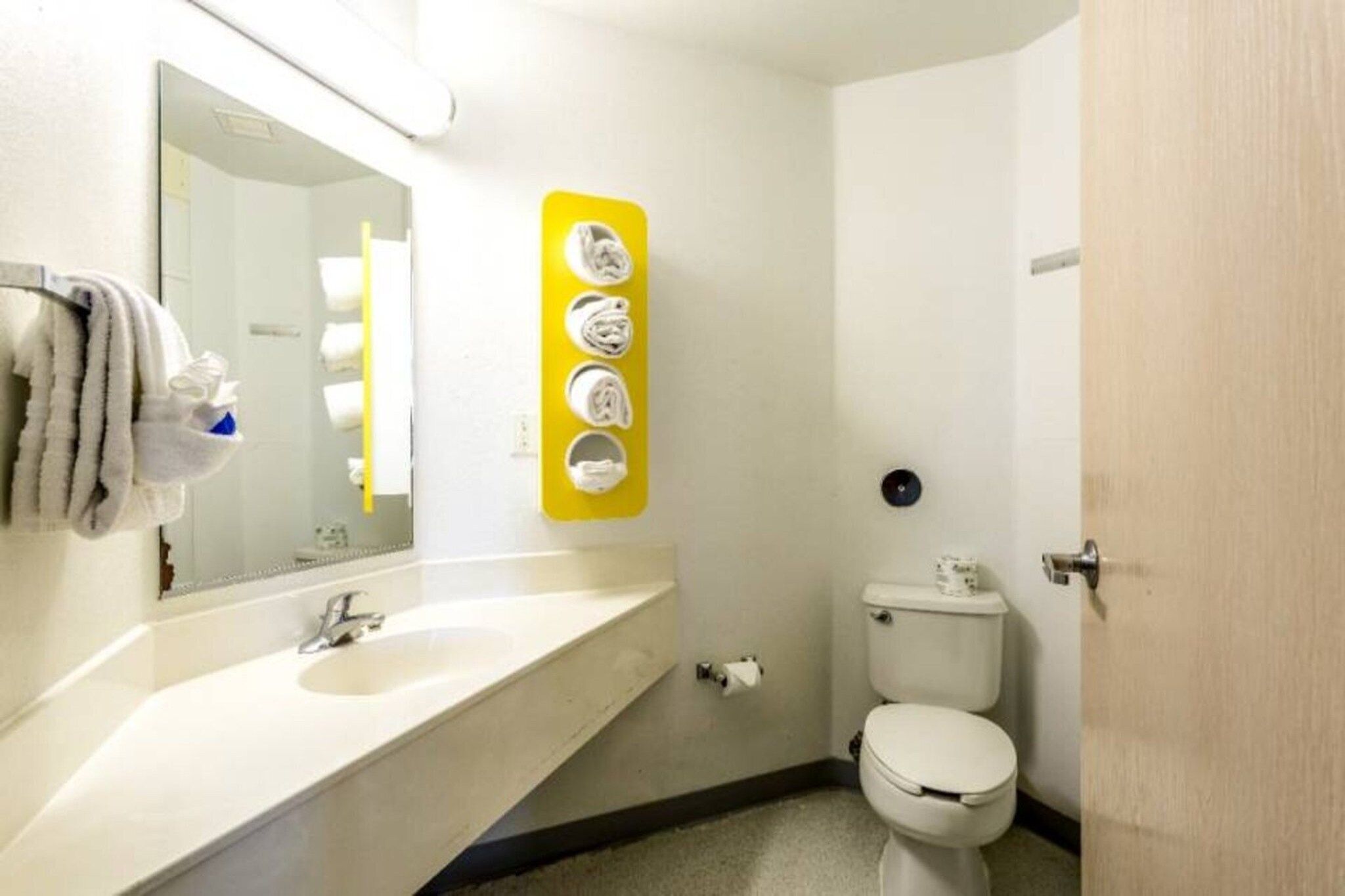 Un baño con lavamanos, espejo, inodoro y un letrero amarillo con símbolos.