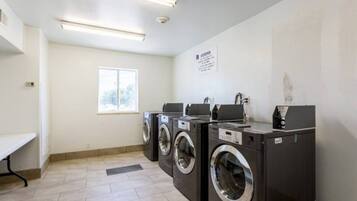 A laundry facility with three washing machines and a bench.