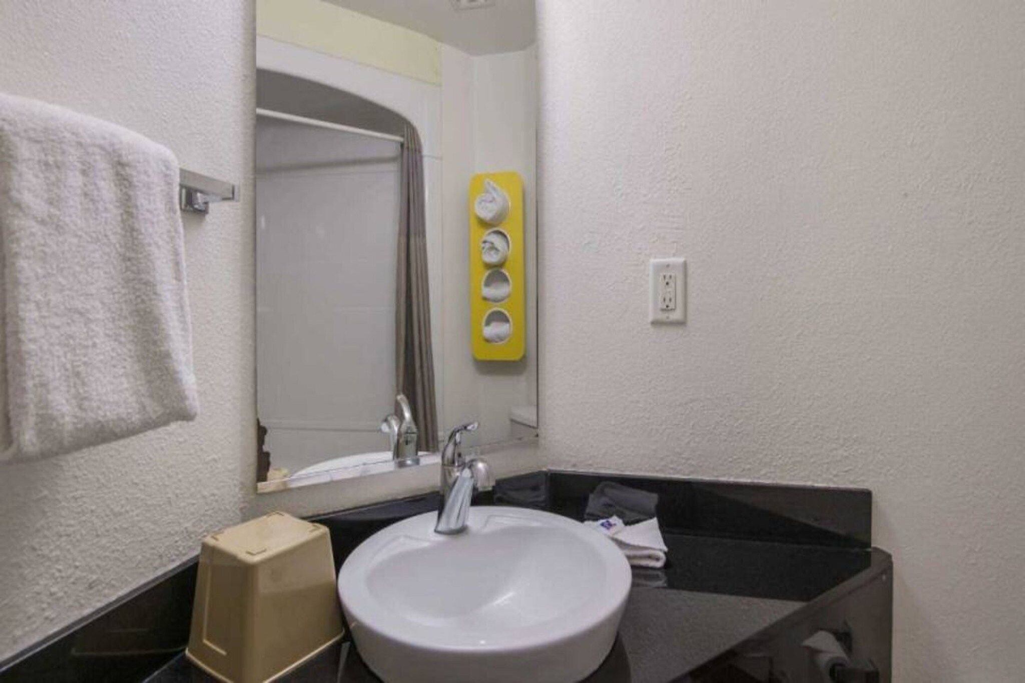 A bathroom with a white sink, a mirror, a towel rack, and a yellow soap dispenser.