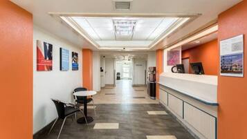 A hotel corridor with a reception desk, chairs, and informational posters on the walls.