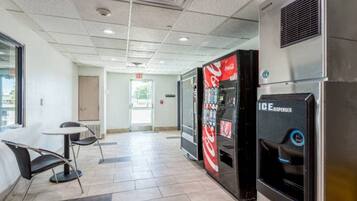 A hotel lobby with a vending machine, a Coca-Cola refrigerator, and a seating area with a table and chairs.