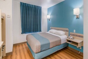 Hotellihuone, jossa on sänky, yöpöytä, lamppu ja ikkuna, jossa on verhot.