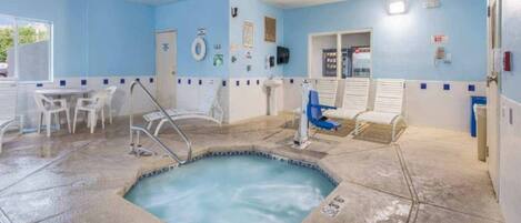 A swimming pool area with a hot tub, lounge chairs, and a small seating area with tables.
