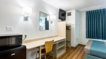 A hotel room with a desk, chair, microwave, TV, wardrobe, and a bed with a blue blanket.