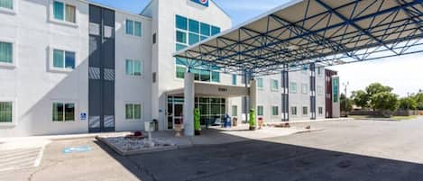 A modern building with a covered entrance, multiple windows, and a visible parking area.