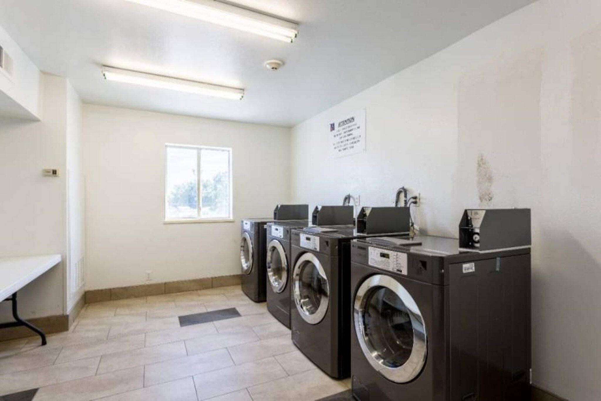 A laundry facility with three washing machines, a bench, and a window.