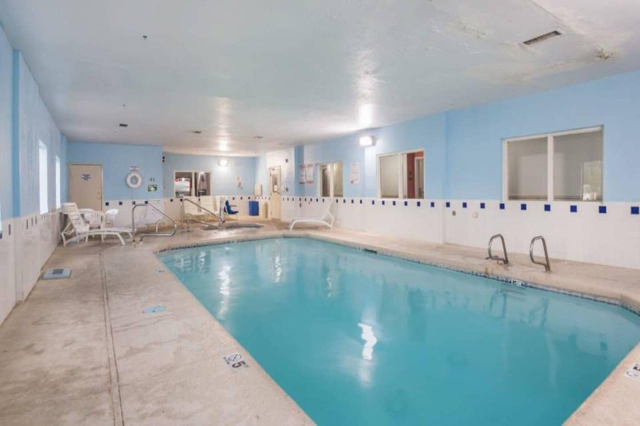 Une piscine intérieure à l’eau claire, entourée de chaises longues et bordée d’un mur carrelé.