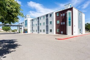 A modern building with a flat roof, multiple windows, and a parking lot in front.