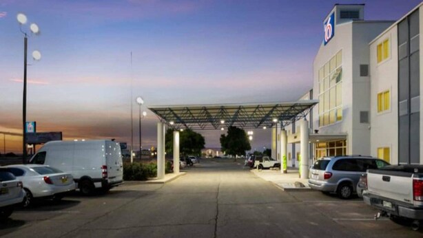 A parking lot with multiple vehicles, a covered area, and a building with a sign. - Cozy 2-bed|Free parking (Roswell)
