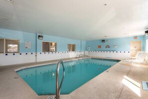 An indoor swimming pool with a tiled floor, a ladder, and a poolside area with chairs.