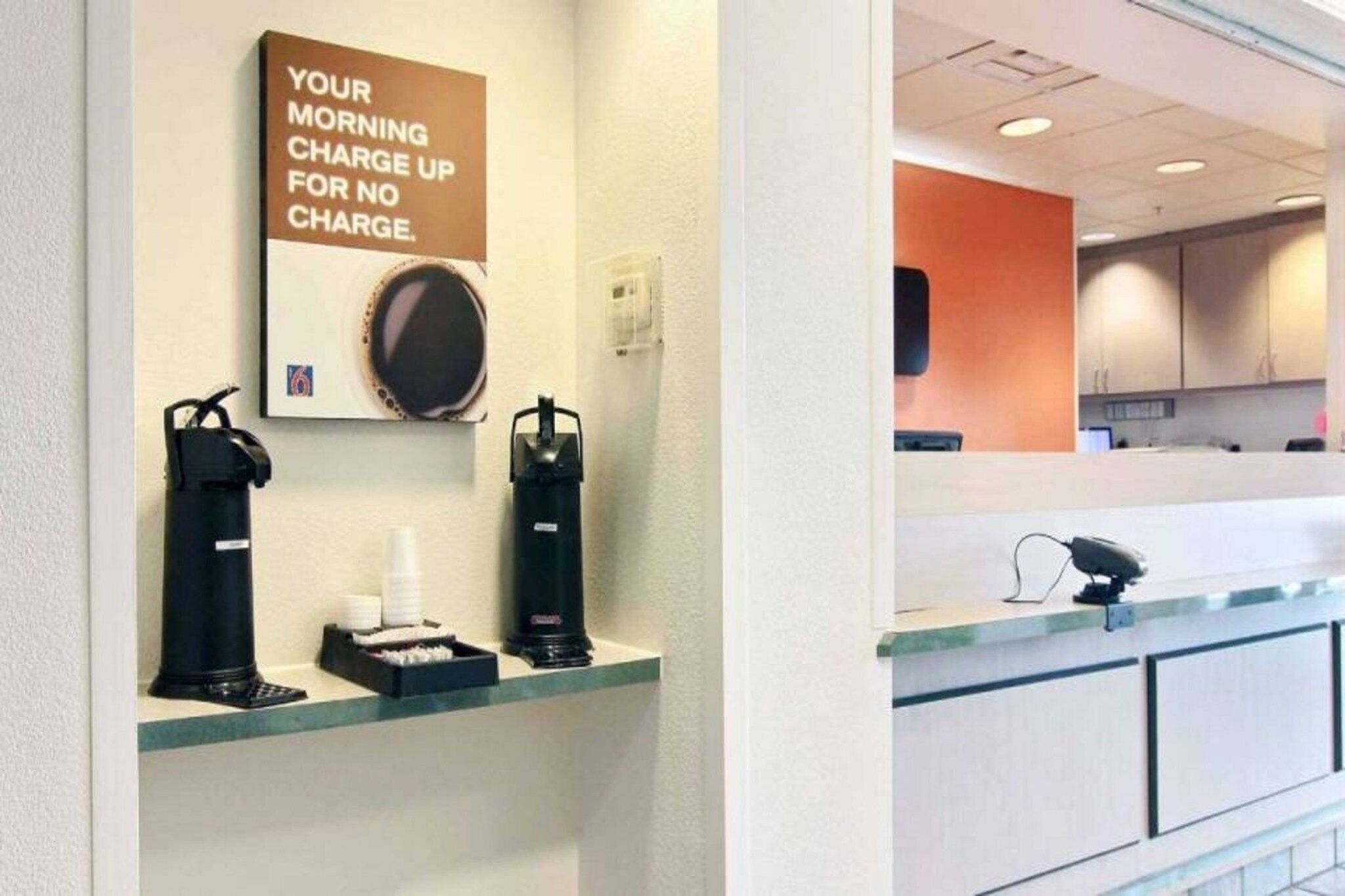 Un'area reception di un hotel con una macchina per caffè, una tazza di caffè e un cartello che recita 'Ricarica mattutina gratuita'.