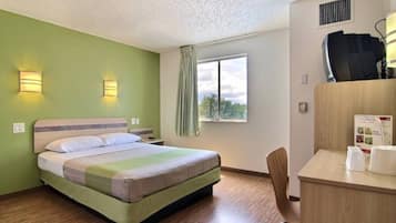 Ein Hotelzimmer mit einem Bett, einem Schreibtisch mit Stuhl, einem Fenster mit Aussicht und einer Wand-Klimaanlage.