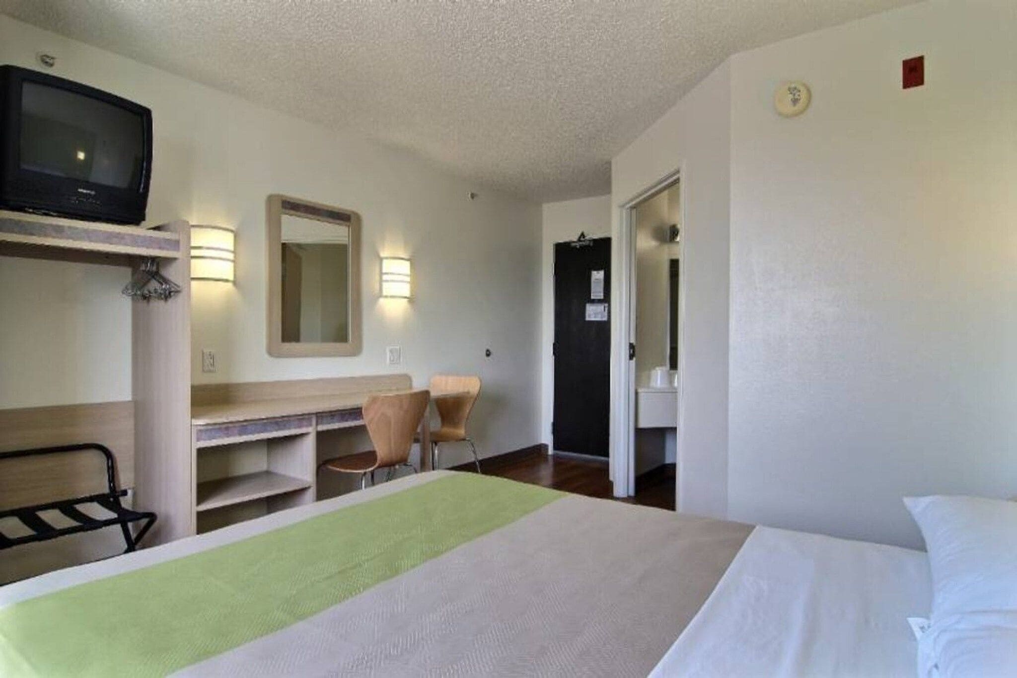 A hotel room with a bed, a desk with a chair, a television, and a mirror.