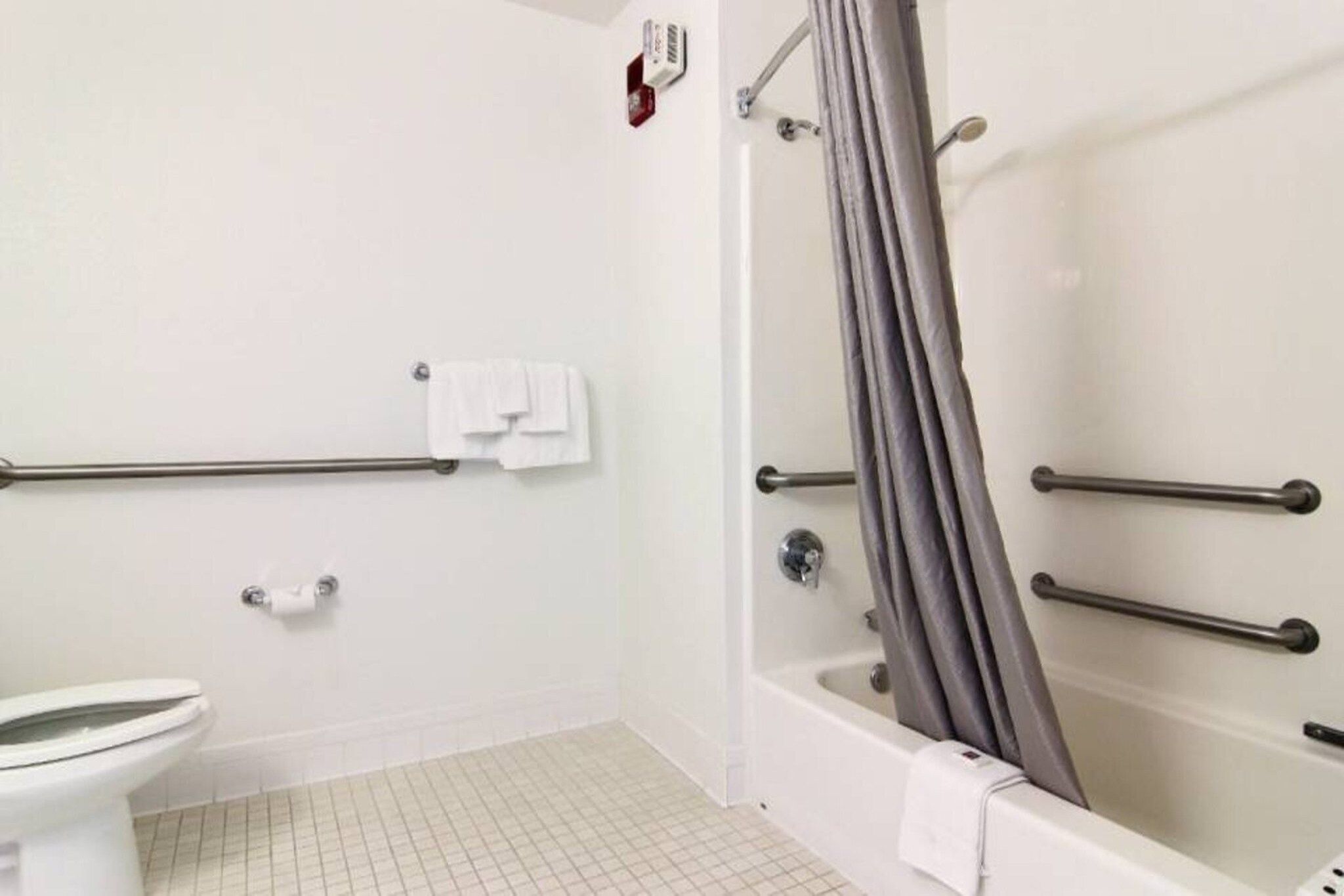 Une salle de bain comprenant des toilettes, une douche équipée d’une barre d’appui et une baignoire.