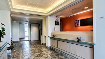 Un espace d’accueil d’hôtel comprenant un comptoir de réception, une horloge et un panneau indiquant l’entrée.