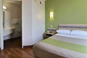 A hotel room with a bed, a bedside table with a lamp, a bathroom with a sink and towel rack. - 1 King Bed | Micfridge (Albuquerque NM)