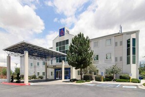 A modern hotel with a covered entrance, a parking lot, and a clear sky. - 1 Full Bed | Non-Smoking (Albuquerque NM)