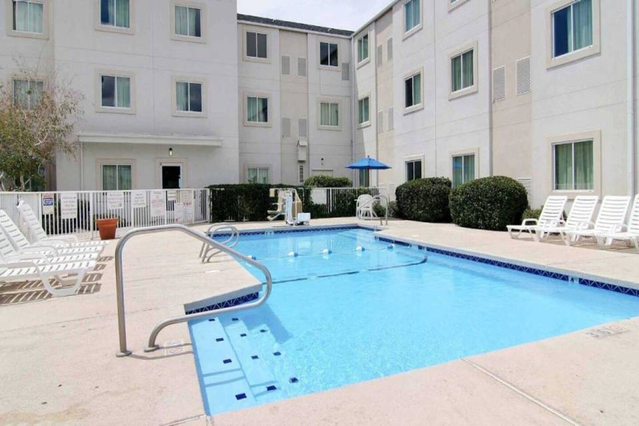 A swimming pool with a diving board, surrounded by lounge chairs and a building with multiple windows.
