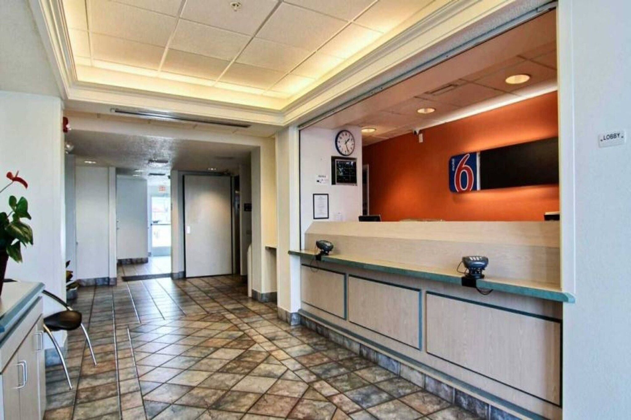 Een hotel receptie met een receptiebalie, een klok en een bordje dat de lobby aangeeft.