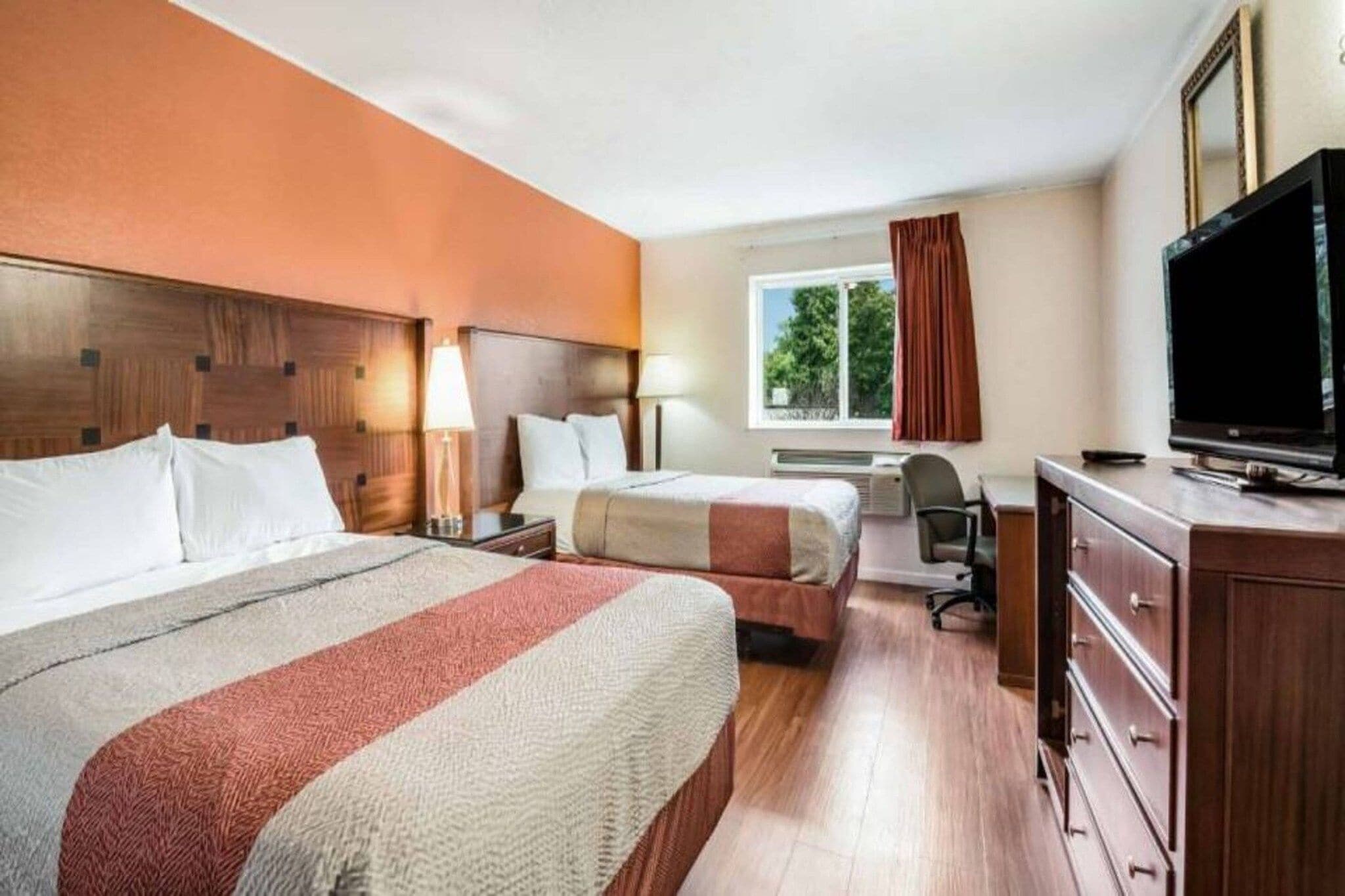 A hotel room with two beds, a television, a desk, and a window with curtains.