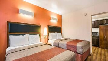 Une chambre d’hôtel avec deux lits, une table de chevet avec une lampe et, au fond, une petite cuisine.