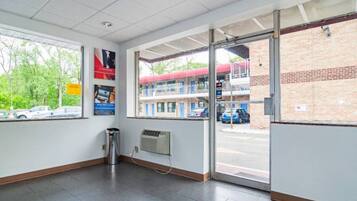 A clean, well-lit interior with a trash bin, a wall-mounted air conditioning unit, and a large window offering a view of the street outside.