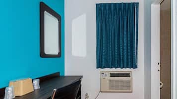 A room with a teal wall, a black-framed mirror, a window with blue curtains, a table with chairs, and a wall-mounted air conditioner.