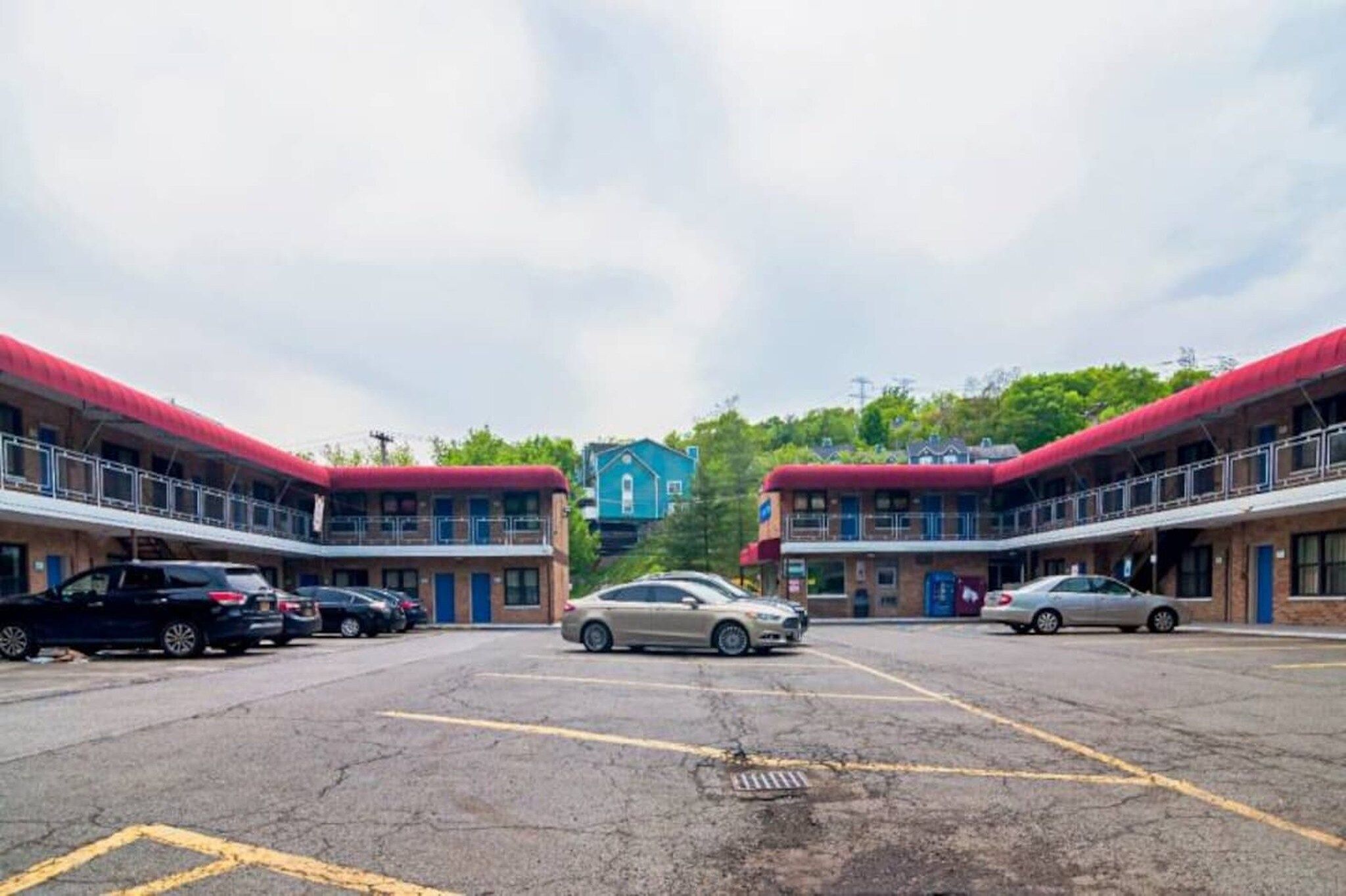 A parking lot with multiple cars, a building with a red roof, and a blue building in the background.