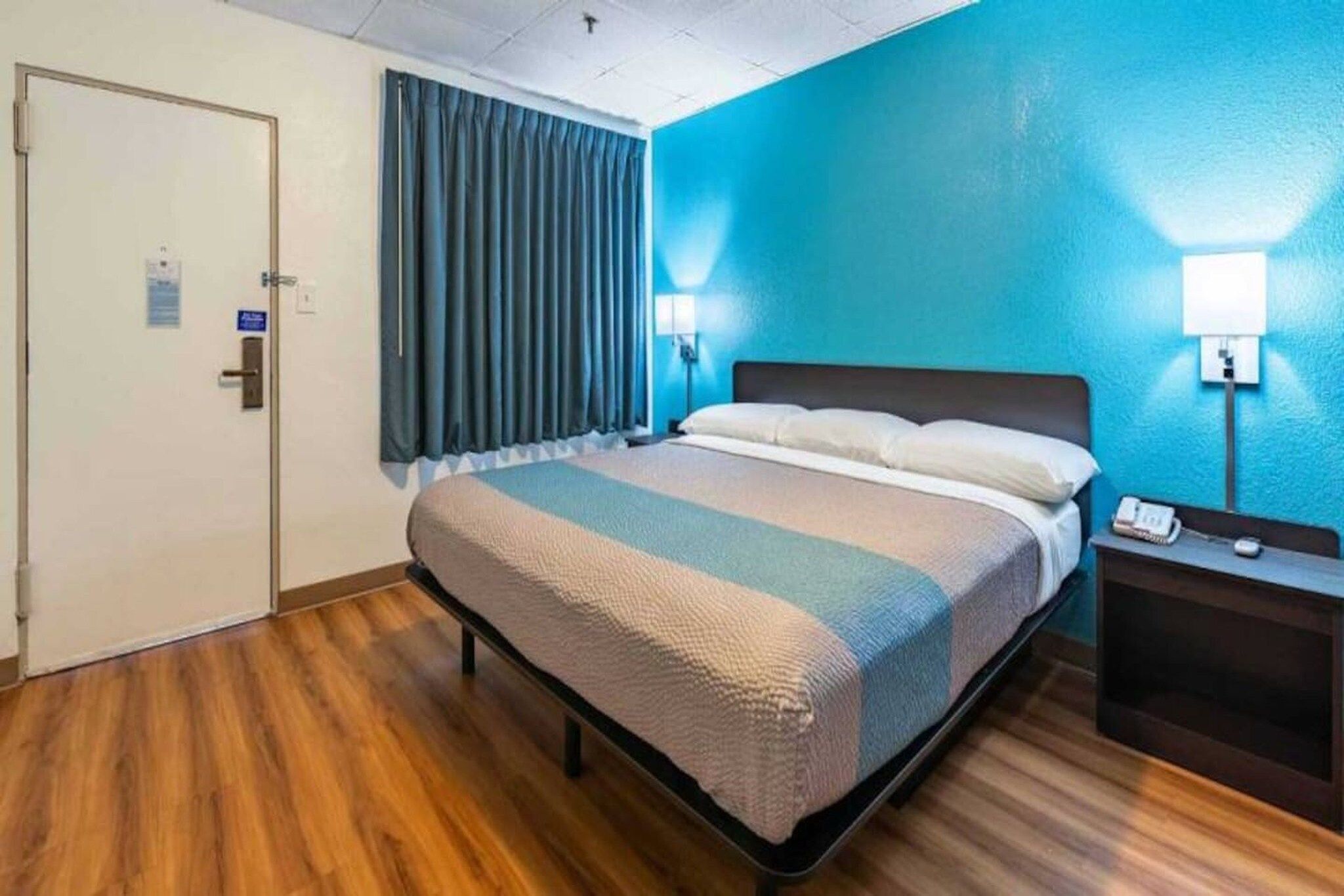 A hotel room with a bed, a nightstand, a lamp, and a door.