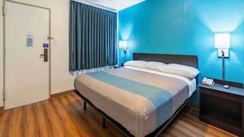 A hotel room with a bed, a nightstand, a lamp, and a door.