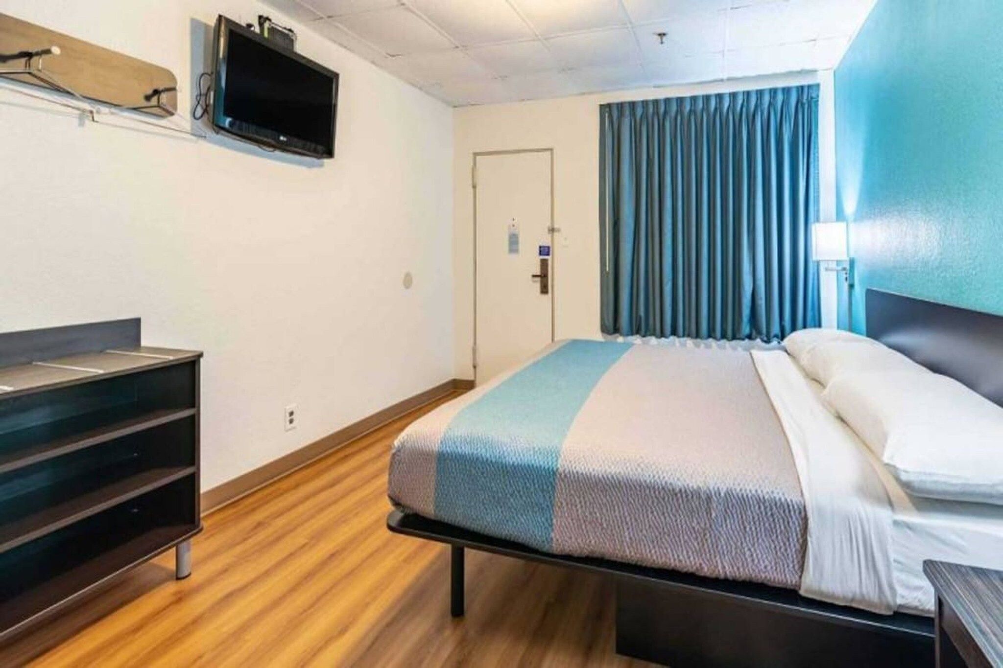 Una habitación de hotel con una cama, un escritorio, un televisor montado en la pared y una puerta con cerradura.