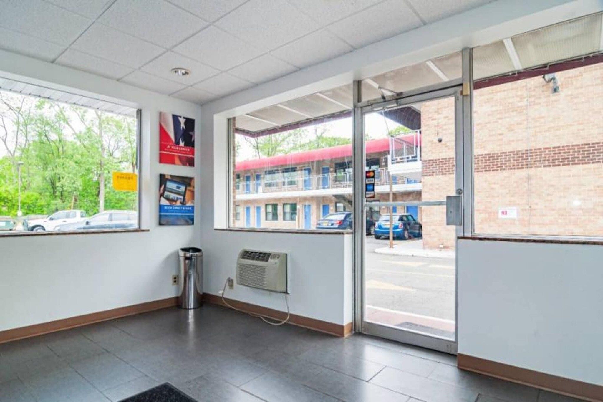 A clean, well-lit indoor space with a trash can, a wall-mounted air conditioning unit, and a door leading outside.