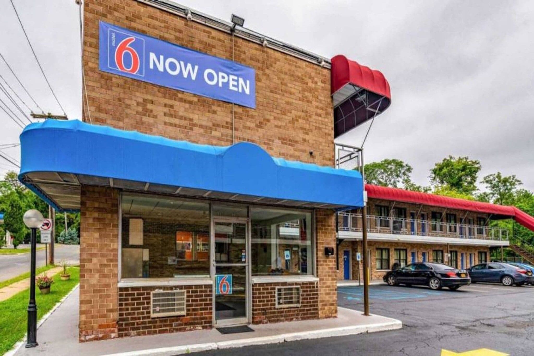 A motel with a blue awning and a '6 Now Open' sign.