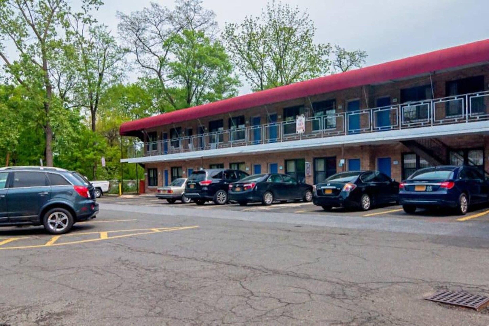 A motel with a red roof, multiple parking spaces, and a balcony on the upper floor.