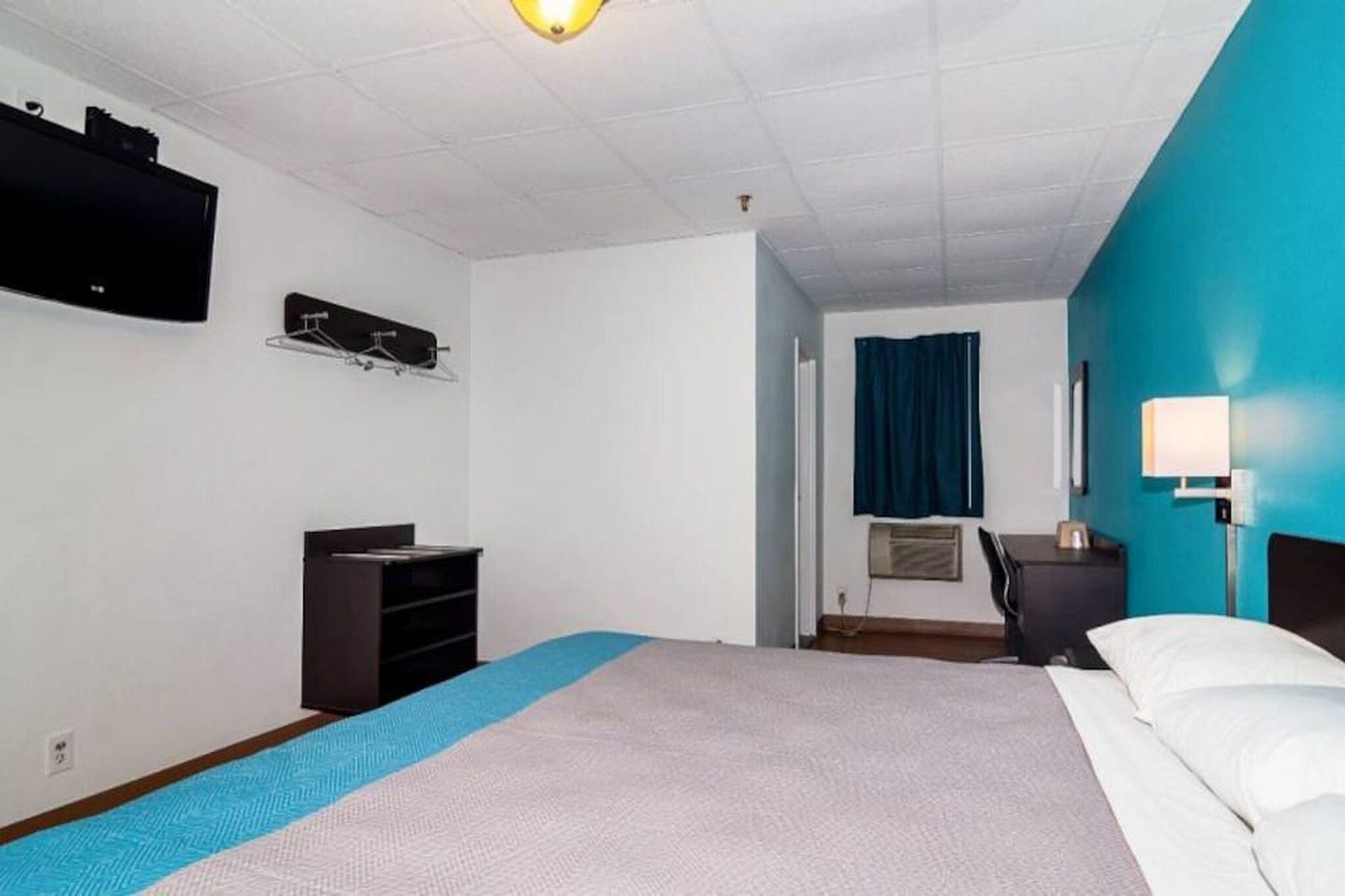 Hotellihuone, jossa on sänky, työpöytä, tuoli, televisio ja ikkuna, jossa on verho.