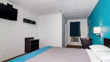 Hotellihuone, jossa on sänky, työpöytä, tuoli, televisio ja ikkuna, jossa on verho.