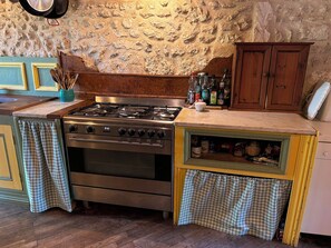 A kitchen with a gas stove, oven, wooden cabinets, and a stone wall. - Large property with privacy and private pool (La Chapelle-Grésignac)