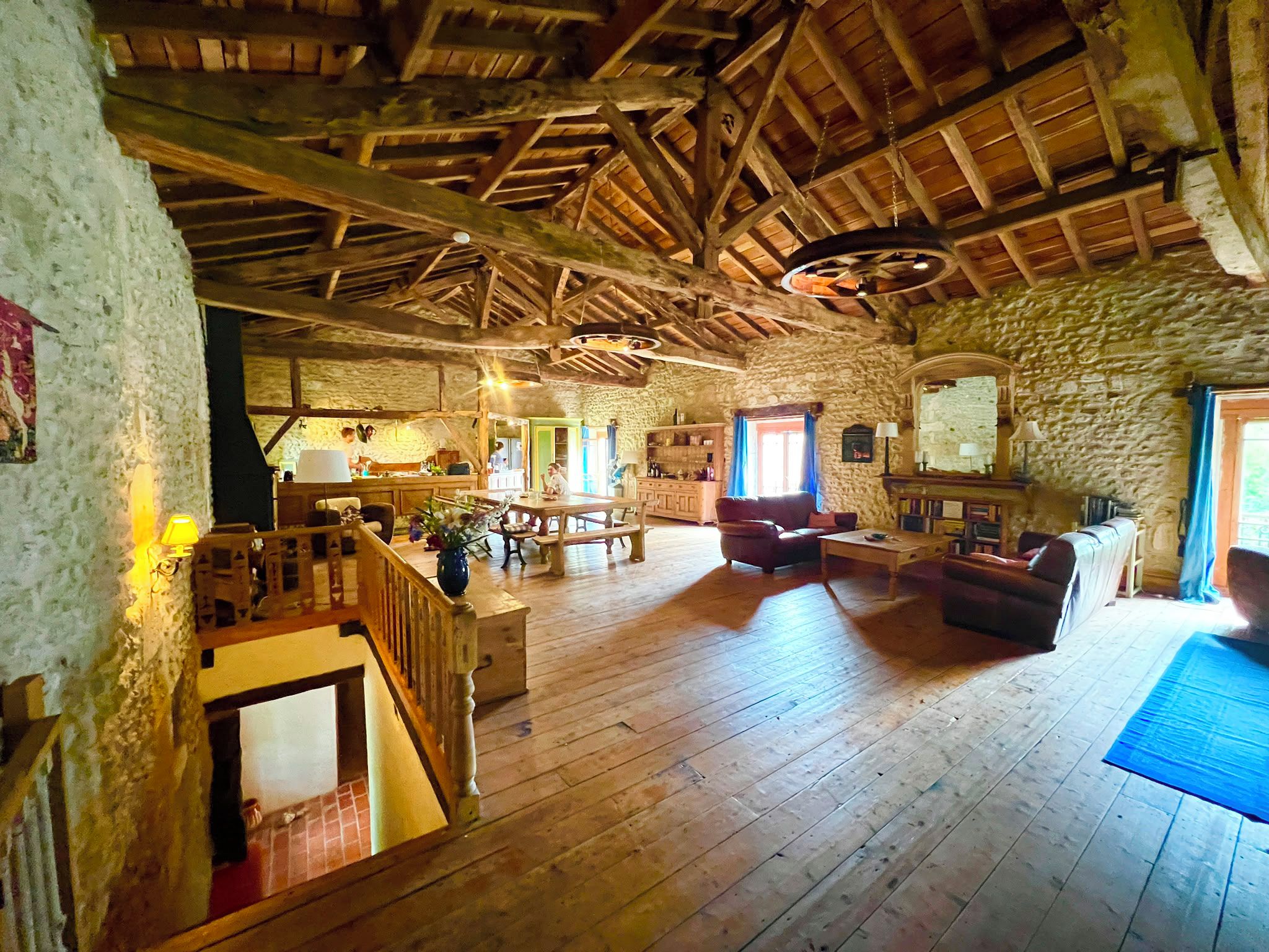 A rustic interior with a wooden floor, stone walls, a dining area, and a staircase.