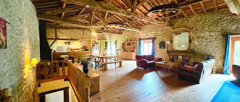 A rustic interior with a wooden floor, stone walls, a dining area, and a staircase.