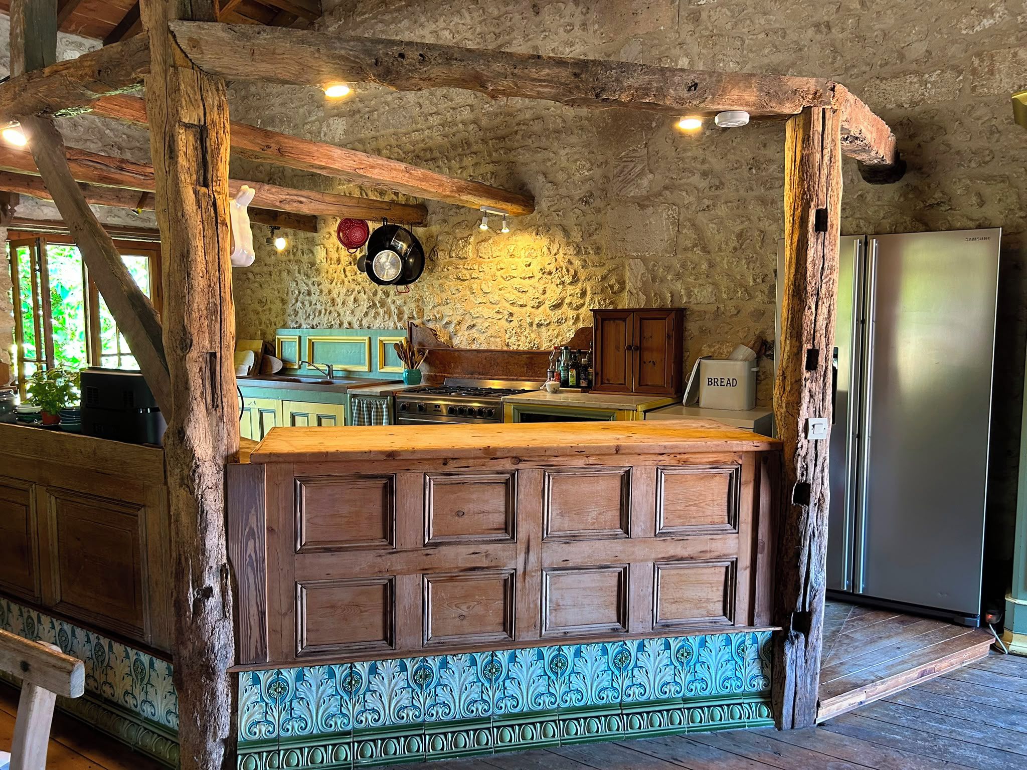 Una cocina rústica con una isla de madera, paredes de piedra y un refrigerador de acero inoxidable.