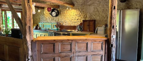 Una cocina rústica con una isla de madera, paredes de piedra y un refrigerador de acero inoxidable.