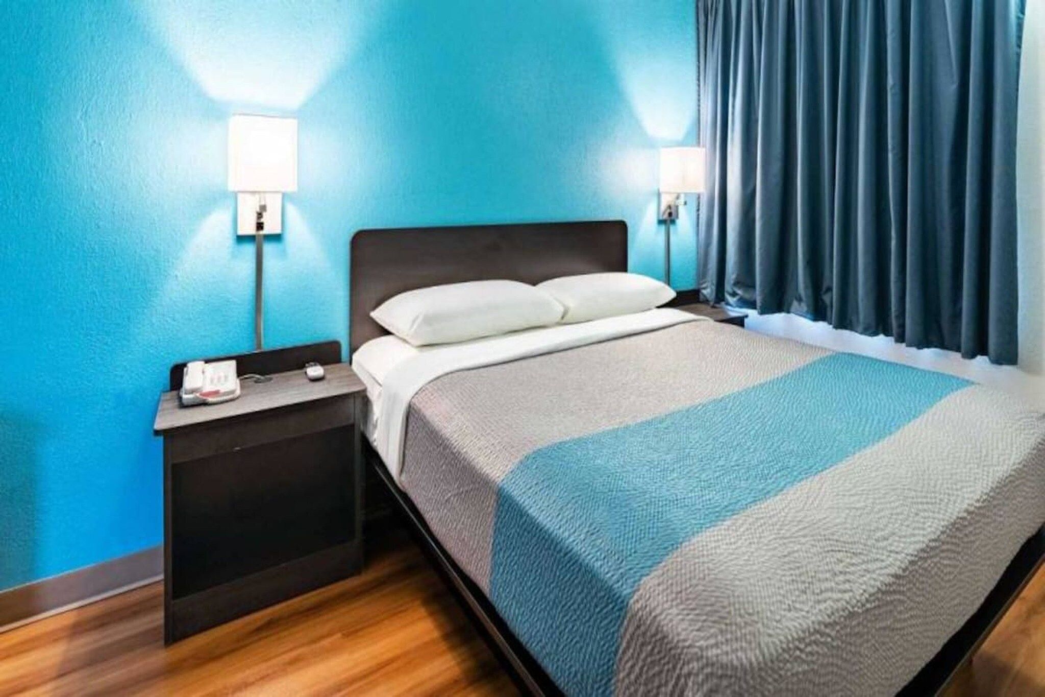 Et hotelværelse med en seng, et natbord, en lampe og gardiner.