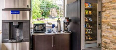 Une petite cuisine équipée d’un distributeur d’eau, d’un four à micro-ondes, d’une machine à café et d’un distributeur automatique de collations.