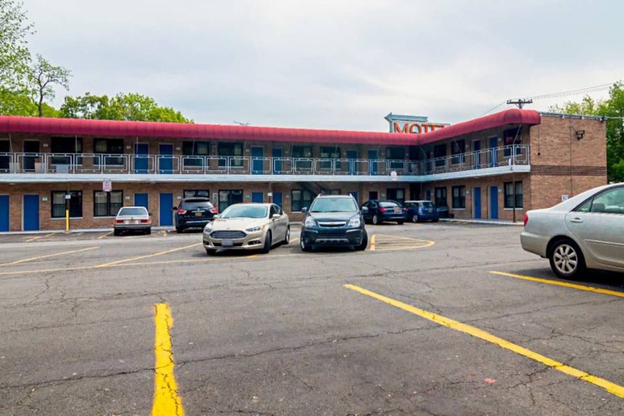 Un motel con techo rojo y estructura de dos pisos. Hay varios coches estacionados en el estacionamiento.