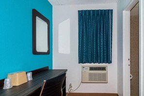 Una habitació amb una taula, cadires, un mirall, una finestra amb cortines i un aparell d'aire condicionat.