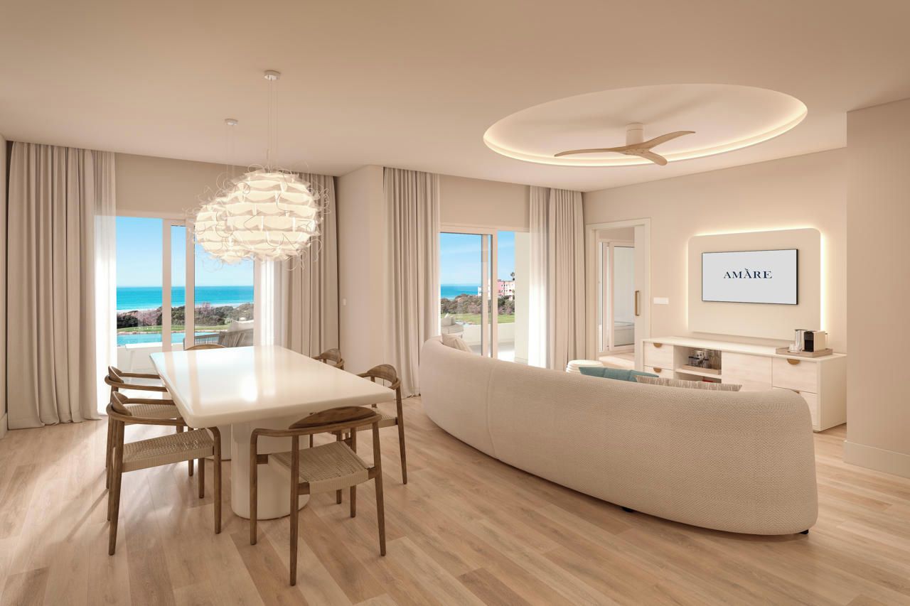 A modern living room with a dining area, a large window with a view, and a flat-screen TV mounted on the wall.